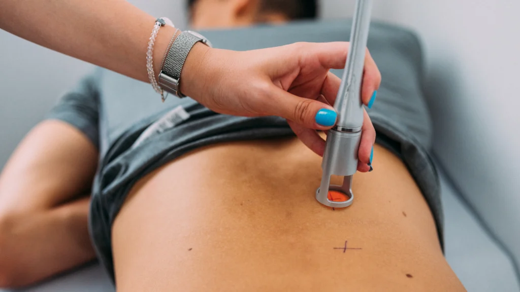 handheld red light therapy machine being used to treat a patients back